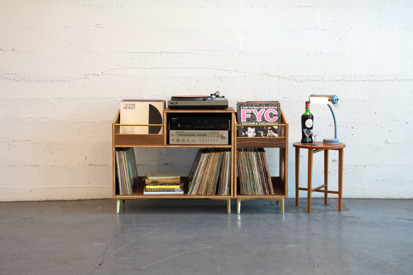 Wooden record player console with vinyl records against a white brick wall.