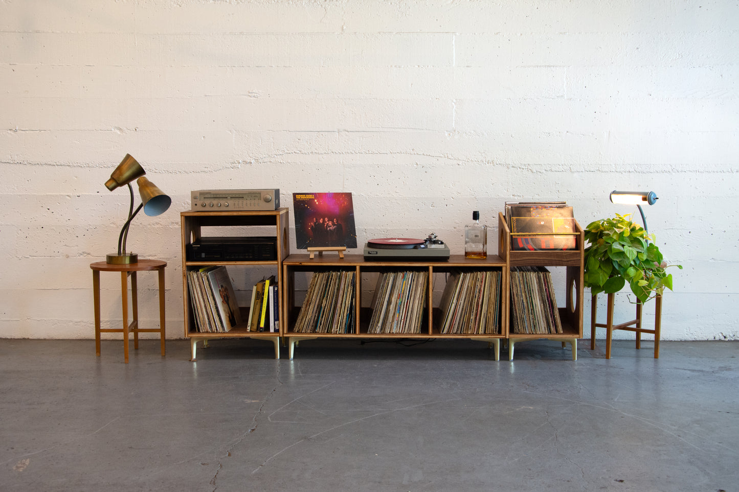 Wooden record player console with vinyl records, speakers, and decorative items against a white brick wall.