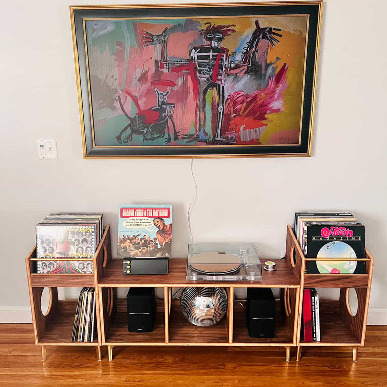 Wooden record player console with vinyl records and a colorful abstract painting above it.