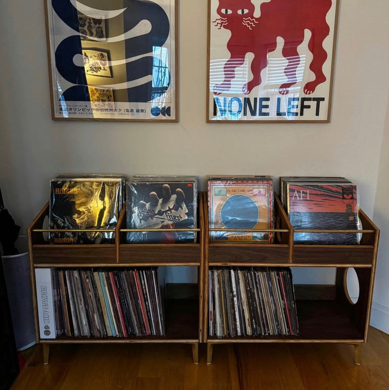 Vinyl records on a shelf with two framed posters on the wall.