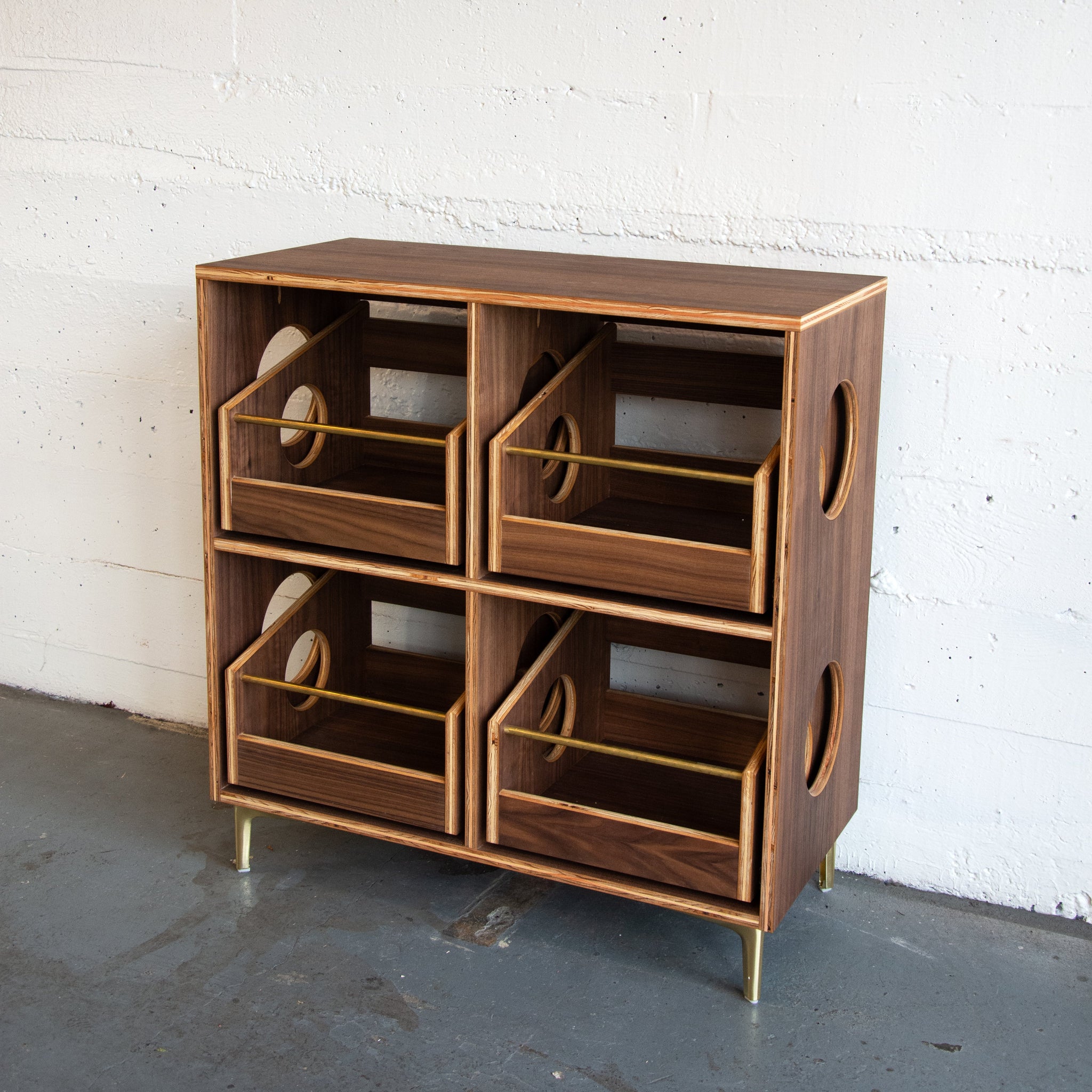 Wooden walnut vinyl cabinet with circular cutouts against a white brick wall.