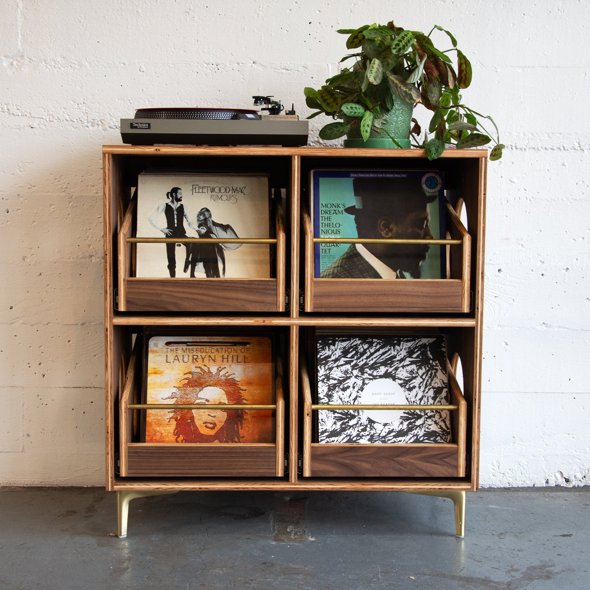 A walnut veneered wood vinyl record storage cabinet with brass accents and four pull-out drawers, set against a white background.