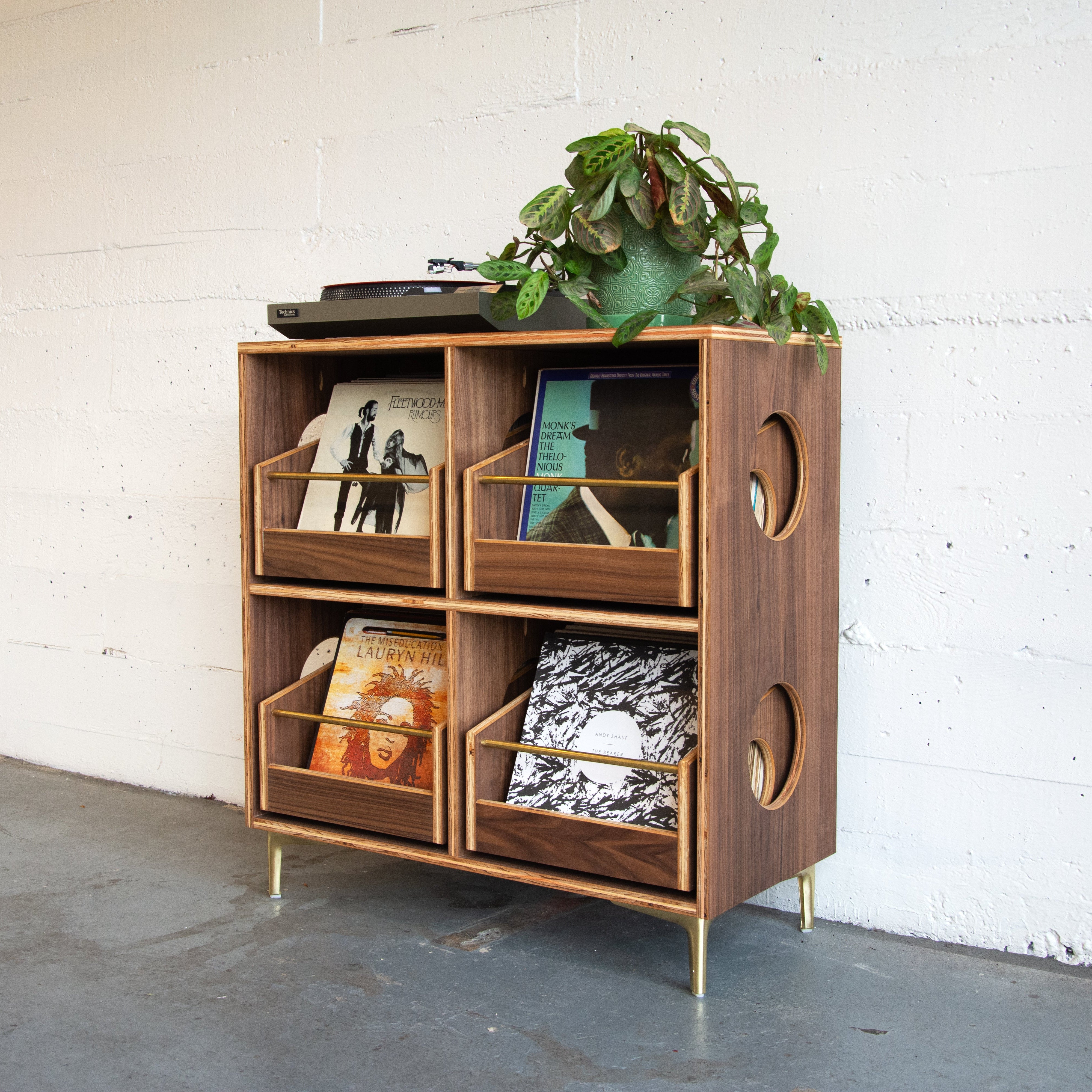 Wooden turntable stand with decorative items against a white brick wall.