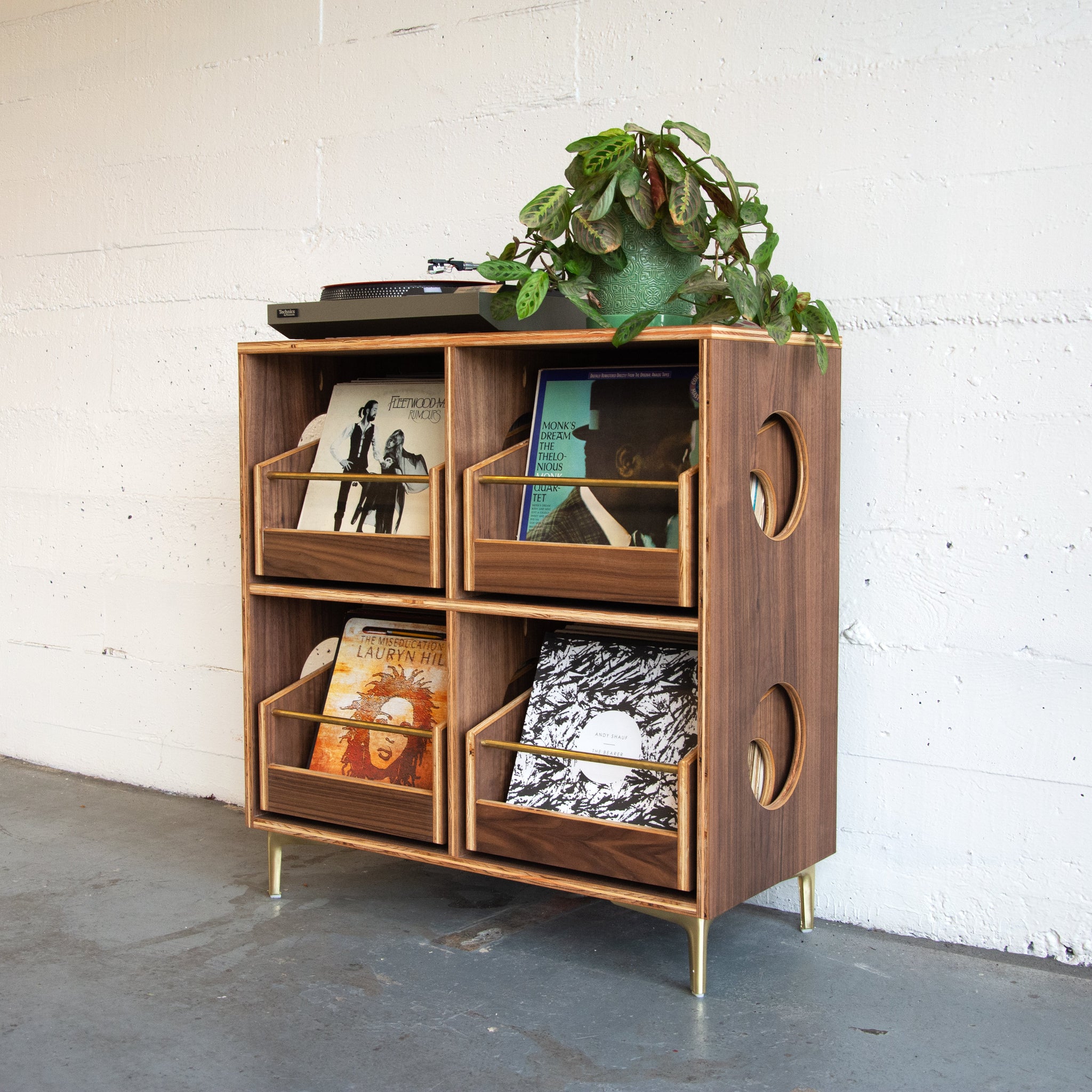 Wooden turntable stand with decorative items against a white brick wall.