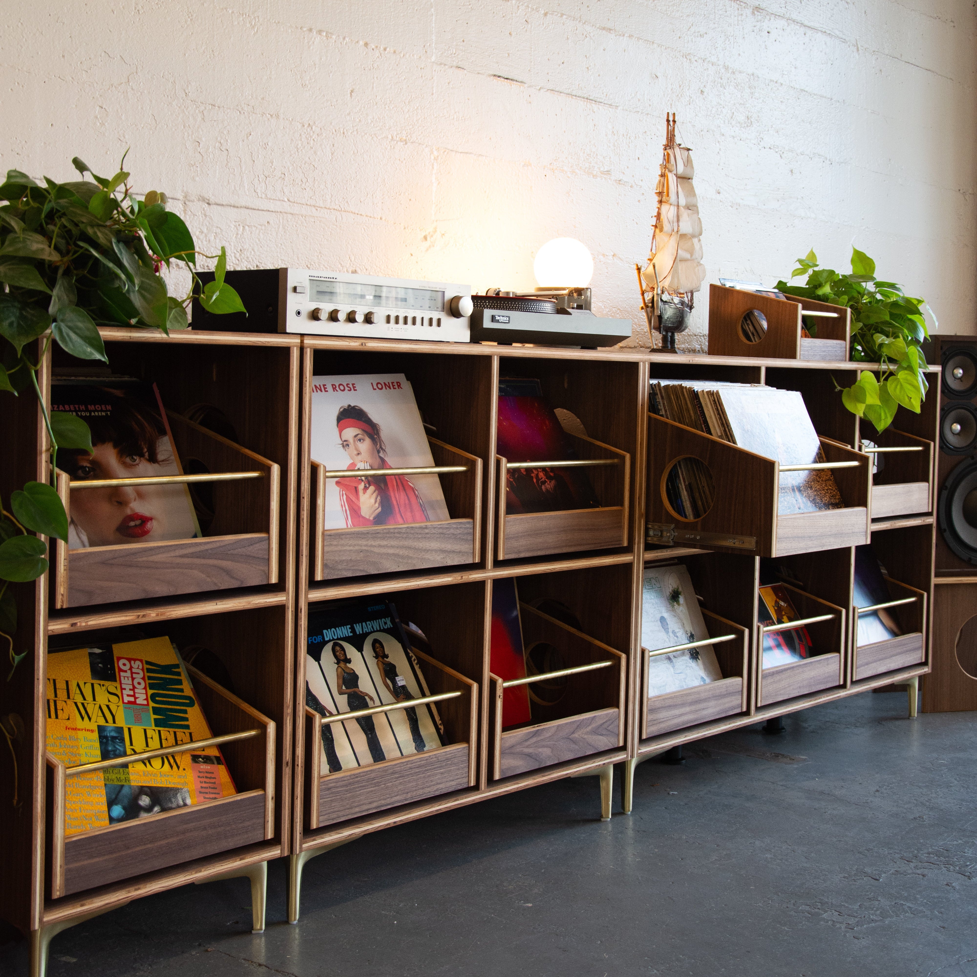 A walnut veneered wood vinyl record storage cabinet with brass accents and four pull-out drawers, set against a white background.