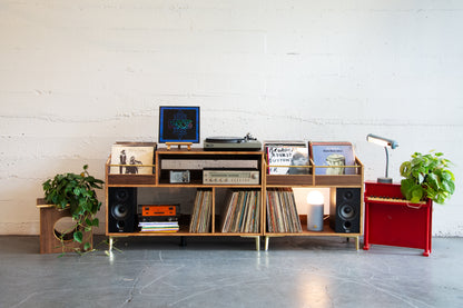 Wooden record player console with vinyl records and speakers in a room with a white wall and gray floor.