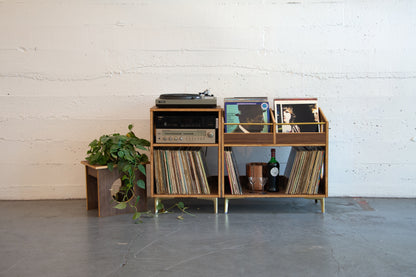 Wooden record player and vinyl collection against a white brick wall.