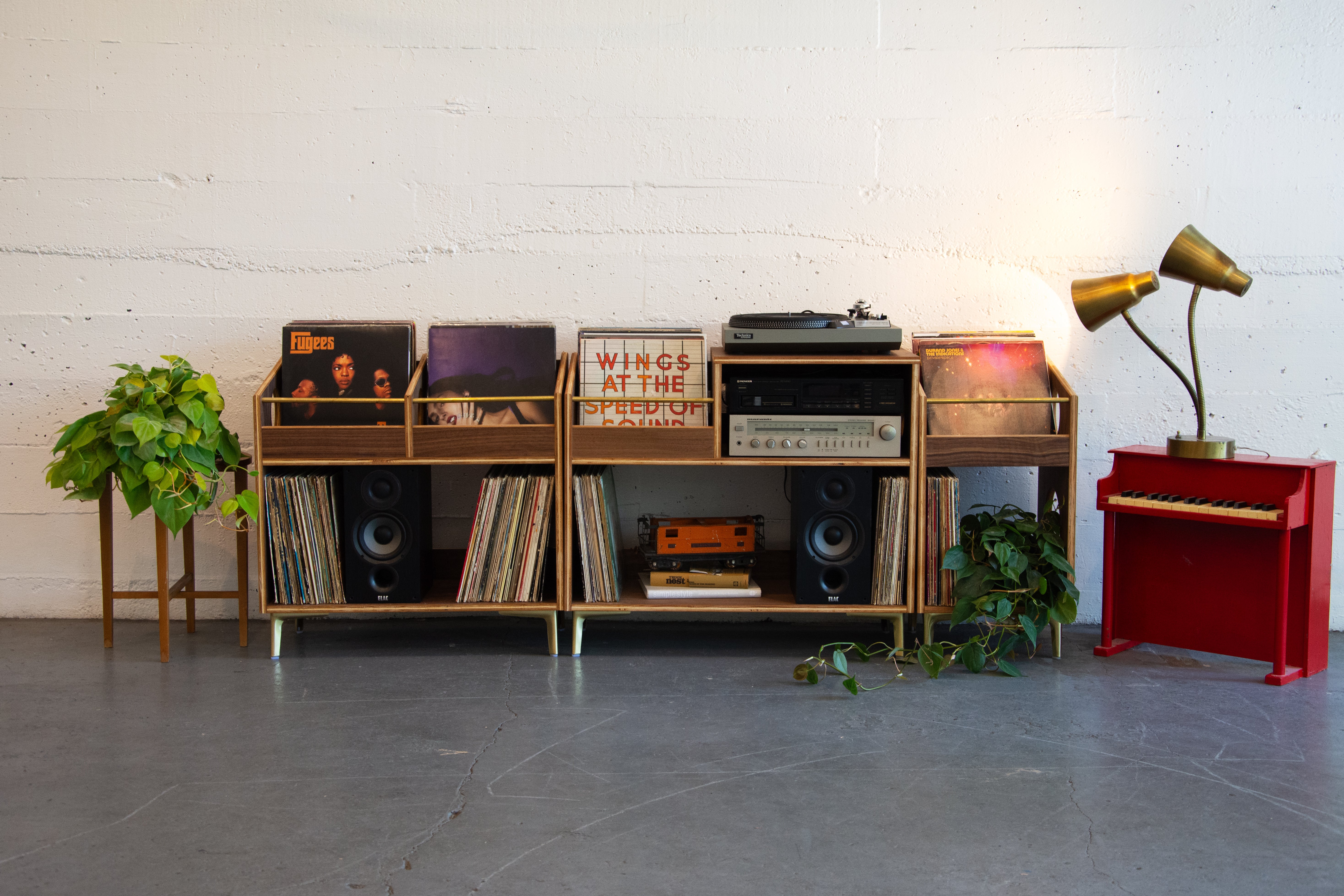 Record player setup with vinyl records, speakers, and a red piano against a white brick wall.