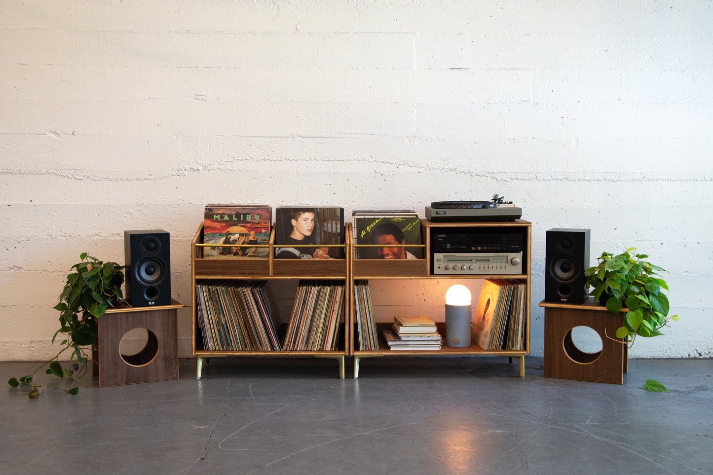 Wooden record player console with vinyl records, speakers, and a lamp against a white brick wall.