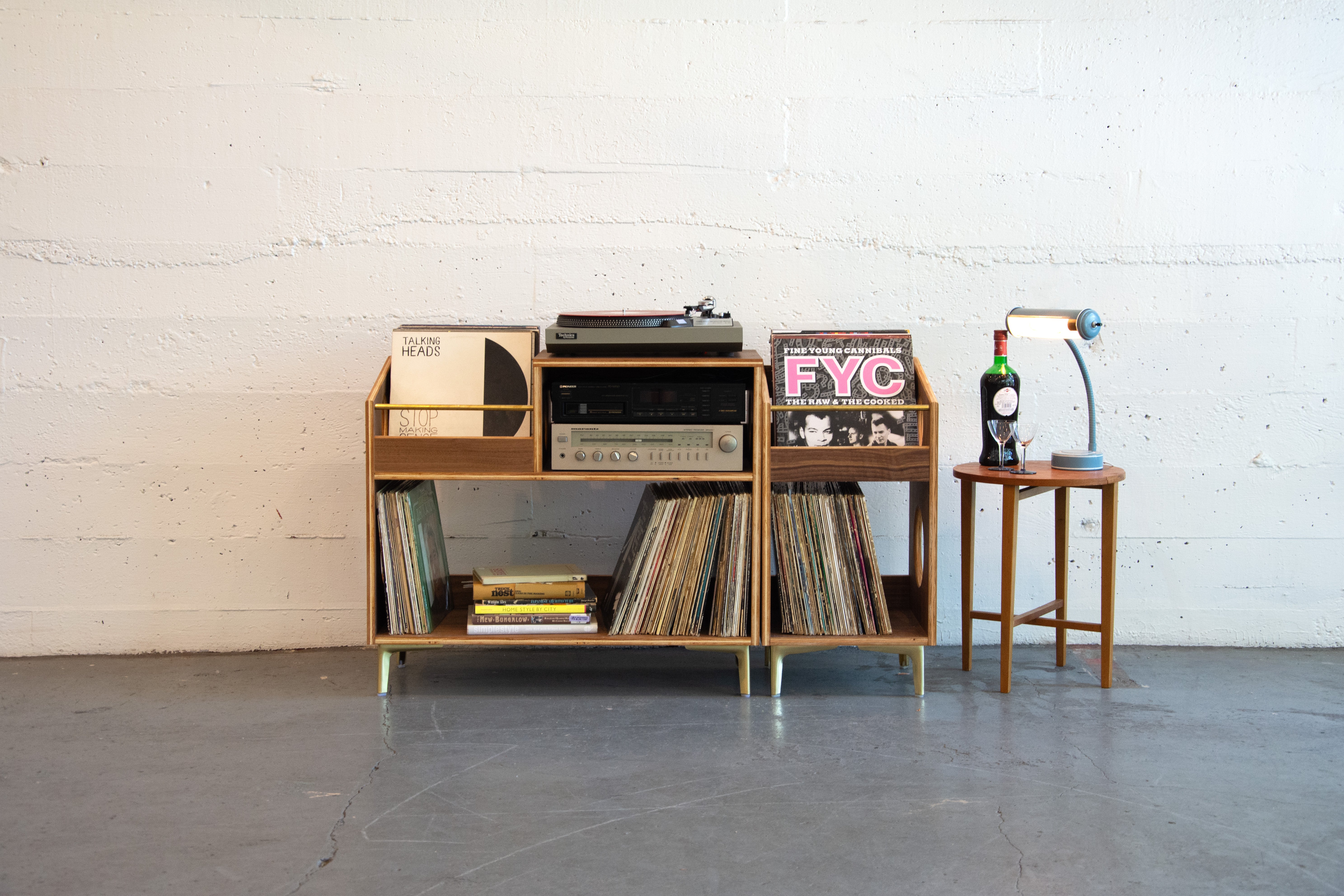 Wooden record player console with vinyl records against a white brick wall.