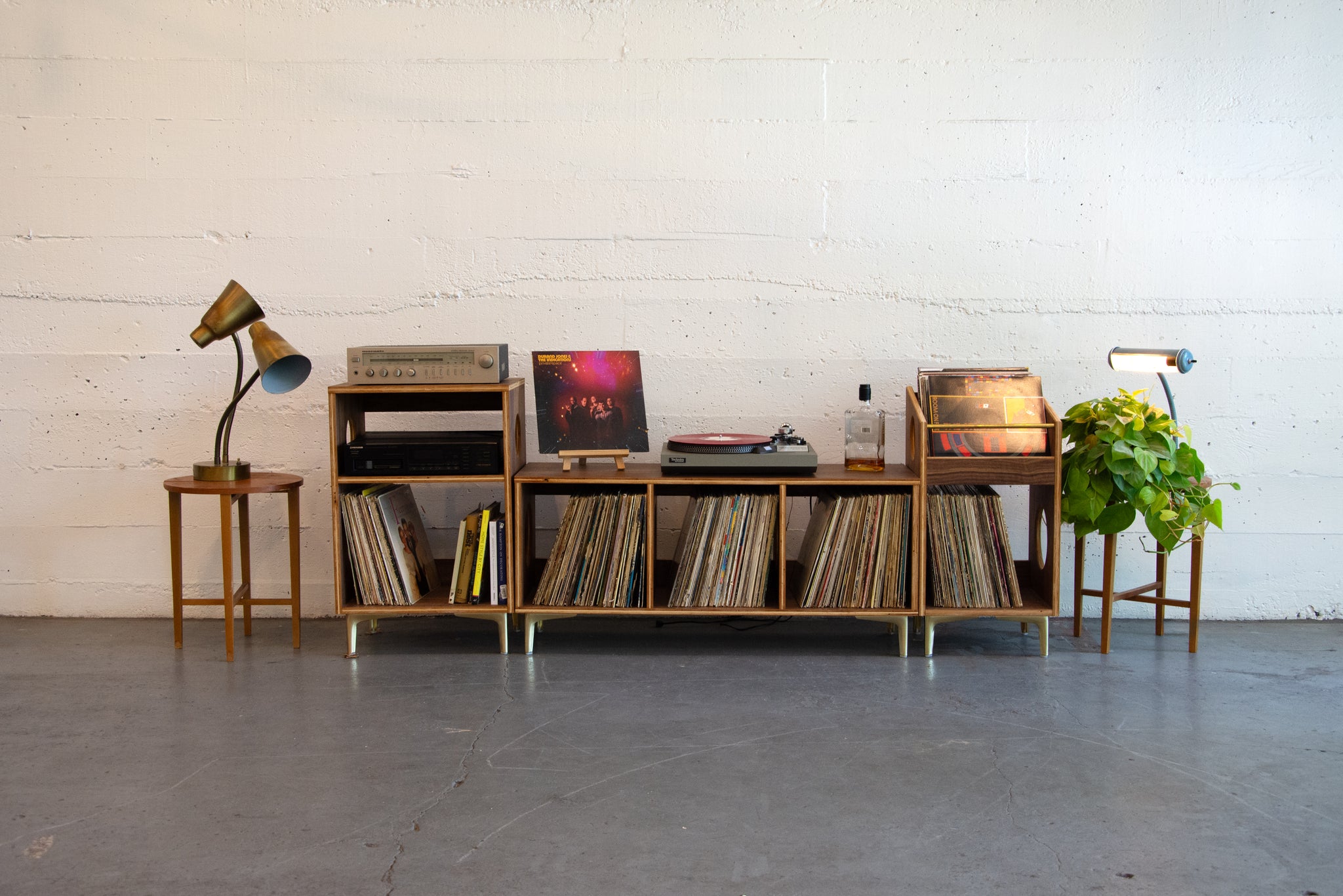 Wooden record player console with vinyl records, speakers, and decorative items against a white brick wall.