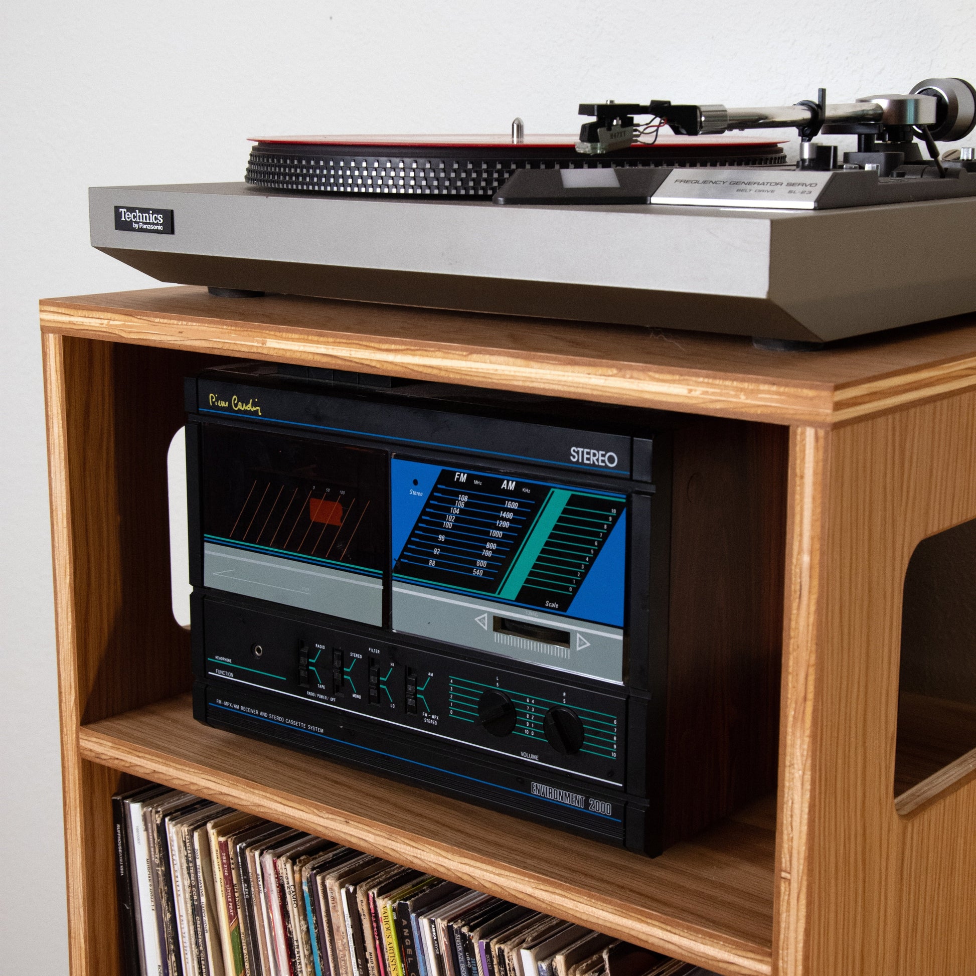 A vintage Steinway turntable sits on top of a wooden record stand holding a black Steinway radio receiver and rows of vinyl records.