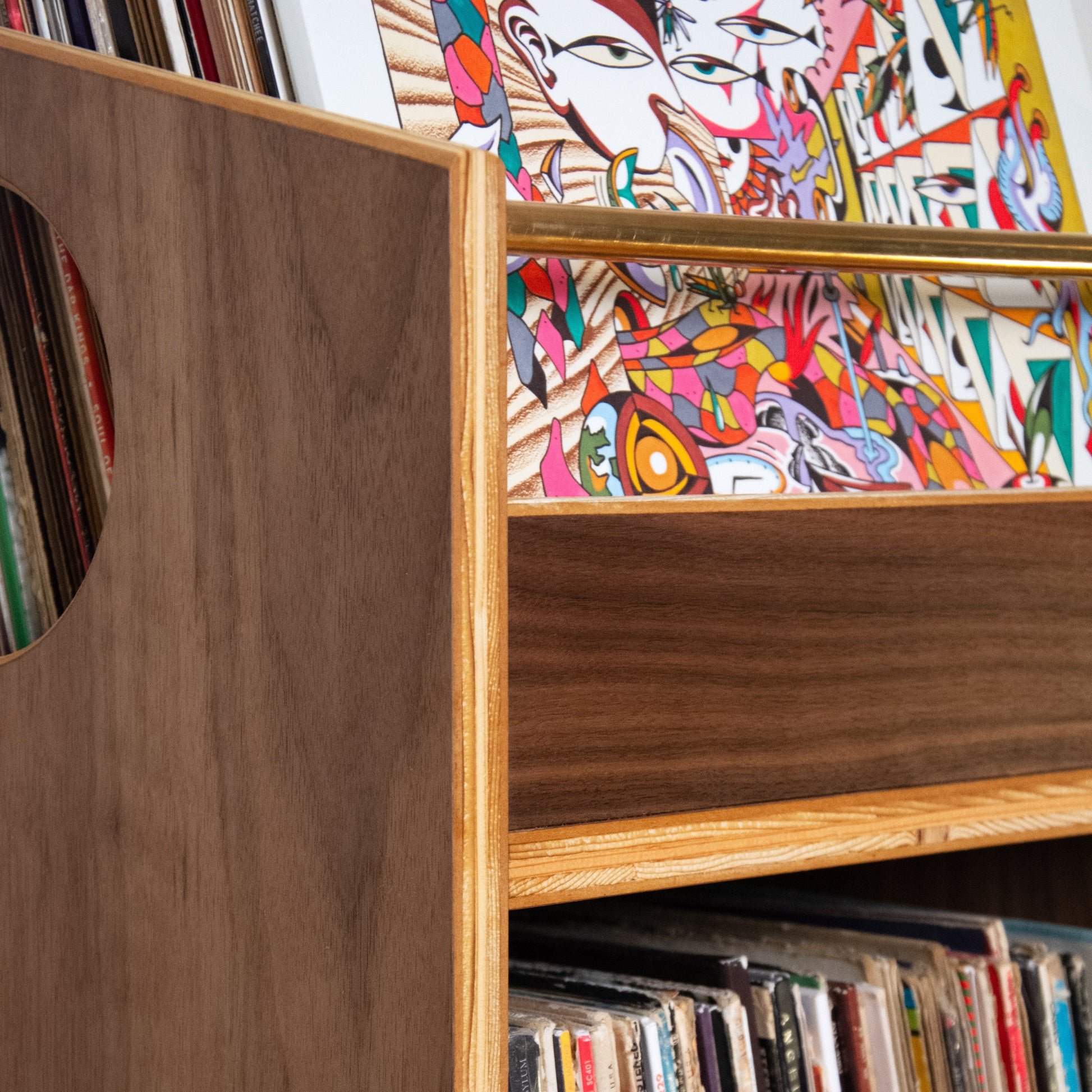 Close-up of a wooden record shelf with vinyl records in a drawer and colorful abstract artwork displayed on the top shelf.