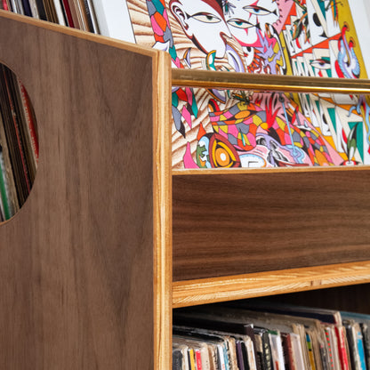 Close-up of a wooden record shelf with vinyl records in a drawer and colorful abstract artwork displayed on the top shelf.