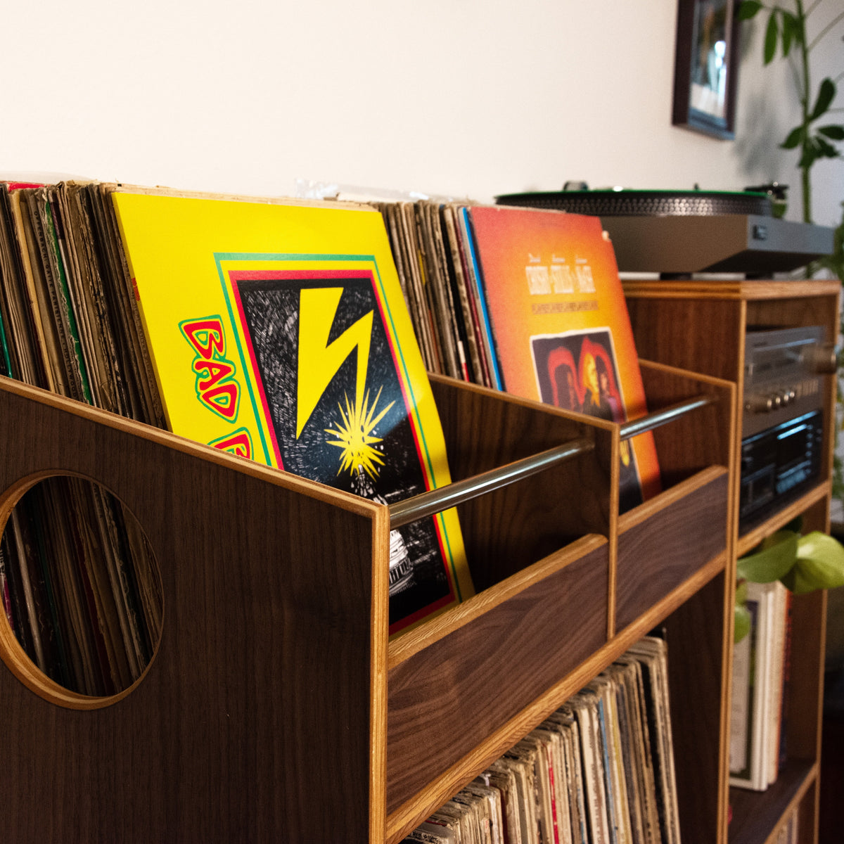 A dark wood vinyl record organizer with a circular cutout, holding various colorful record sleeves, shown in a home interior setting.