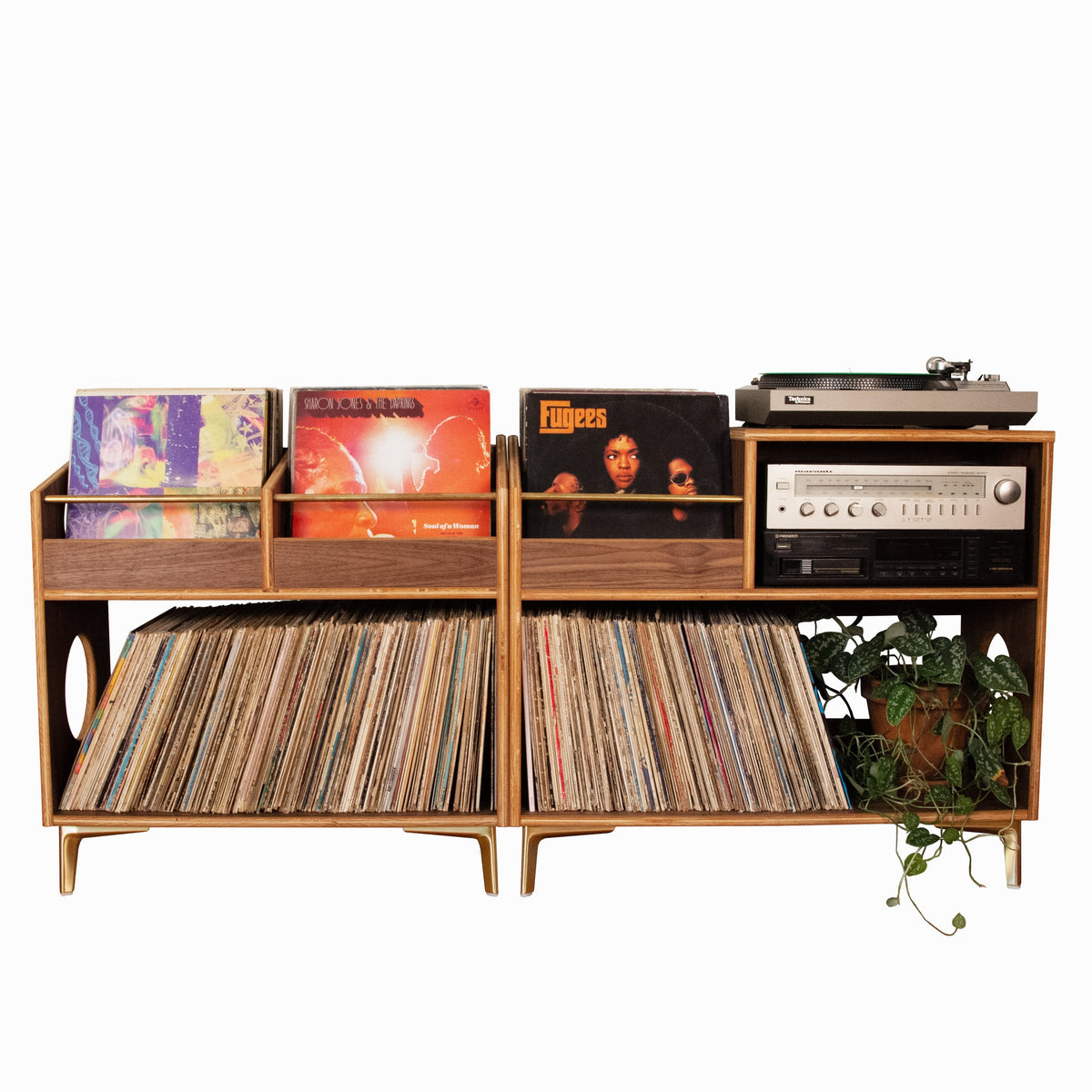 A mid-century modern wooden record shelf and media console with gold-tone legs, holding vinyl records, record sleeves, a turntable, and an audio receiver, isolated on a white background.