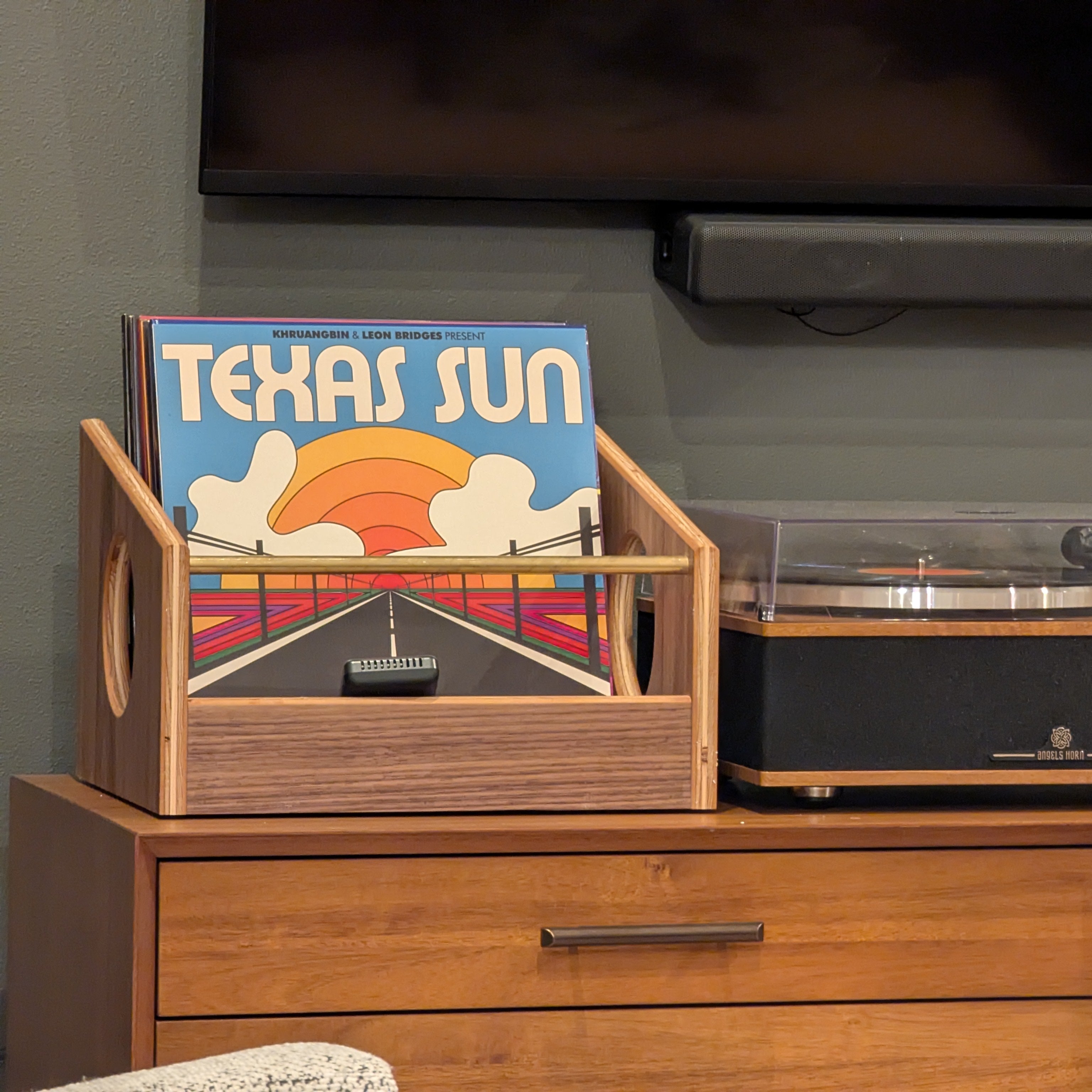 Record player with vinyl records on a wooden cabinet against a gray wall.