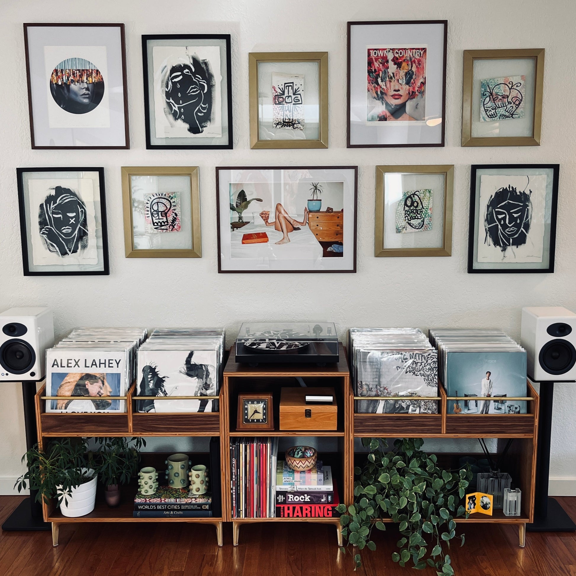 Music collection with vinyl records and speakers on a wooden shelf against a wall with framed artwork.