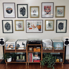 Load image into Gallery viewer, Music collection with vinyl records and speakers on a wooden shelf against a wall with framed artwork.
