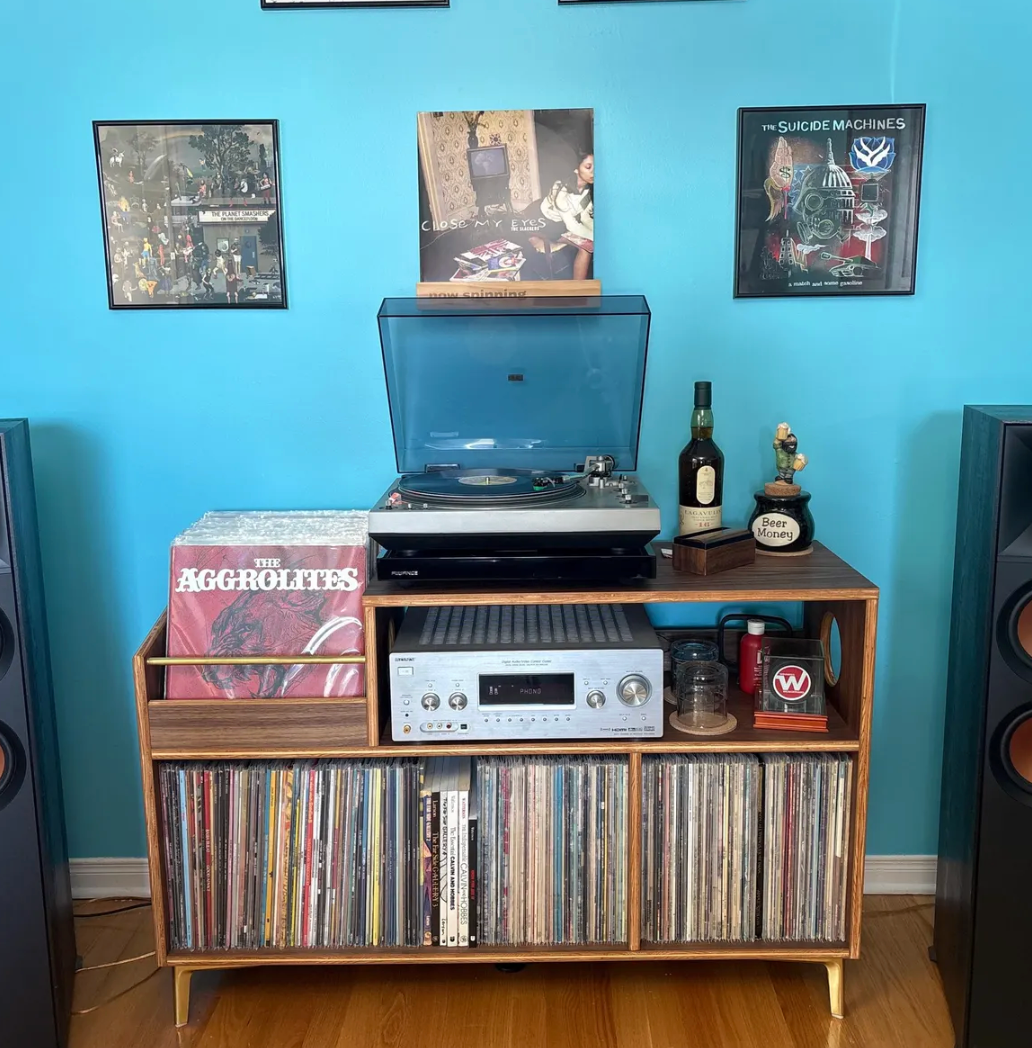 Wooden record player console with vinyl records against a blue wall.