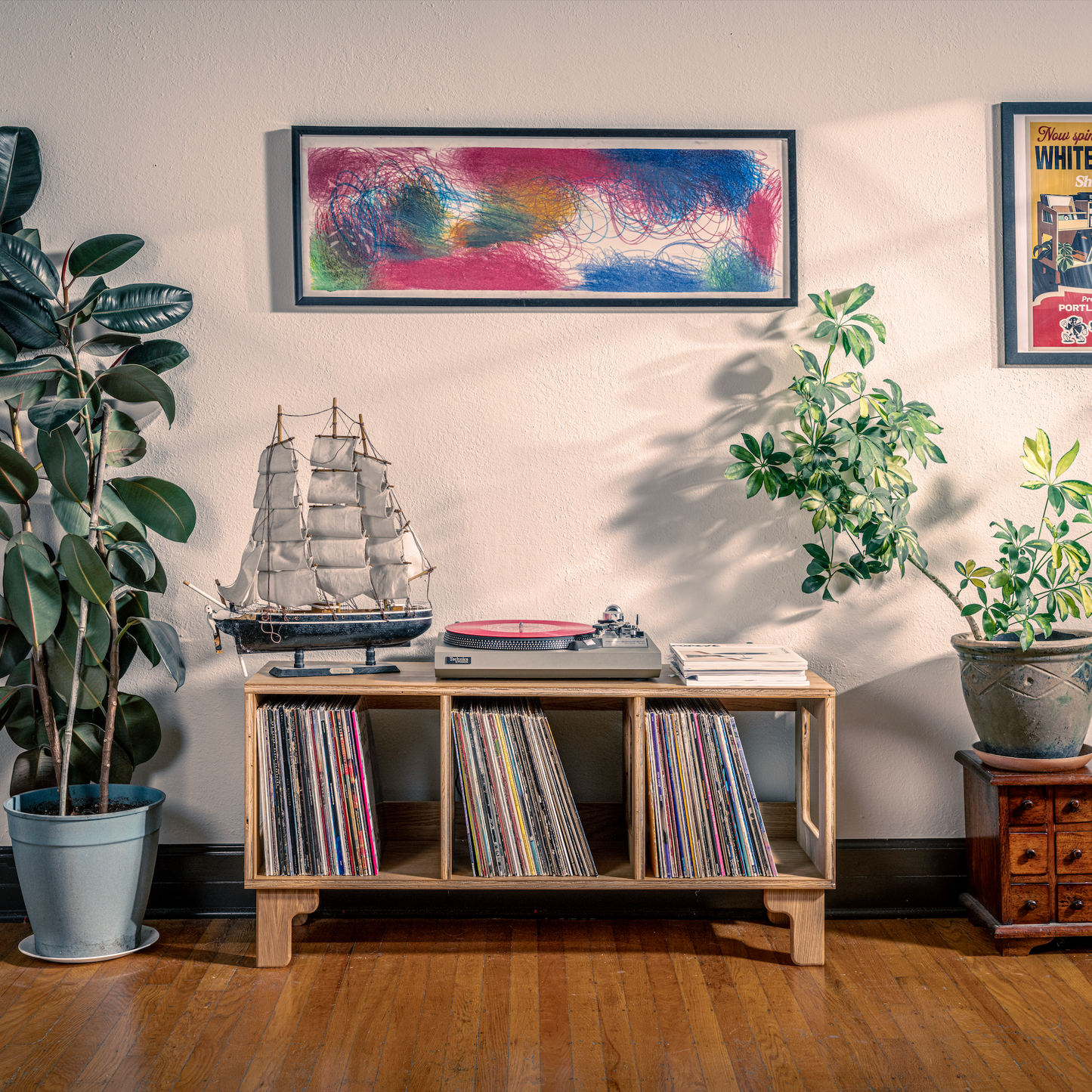 Room interior with vinyl records, a ship model, and plants on a wooden shelf.