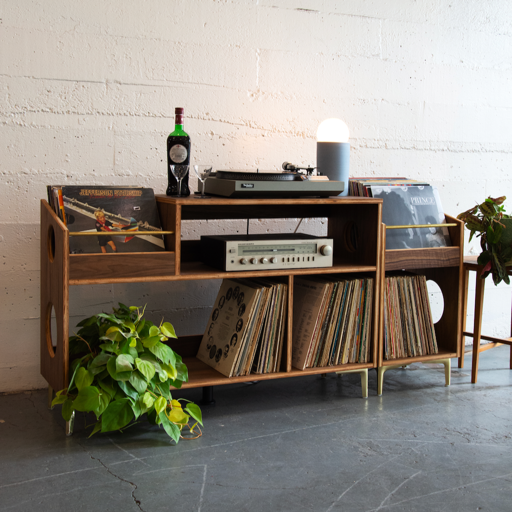 Wooden record player console with vinyl records against a white brick wall.