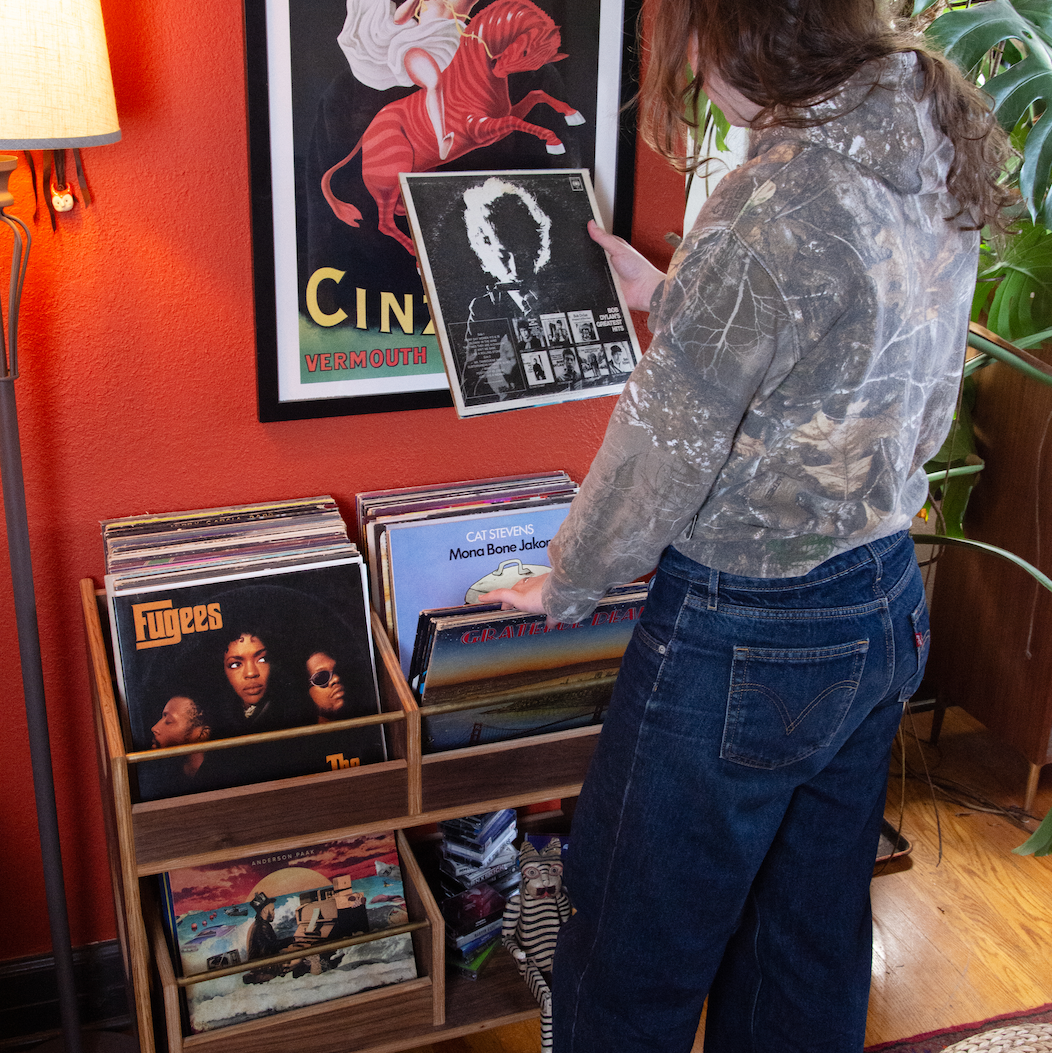 Person browsing vinyl records in a room with a red wall, posters, and a lamp.