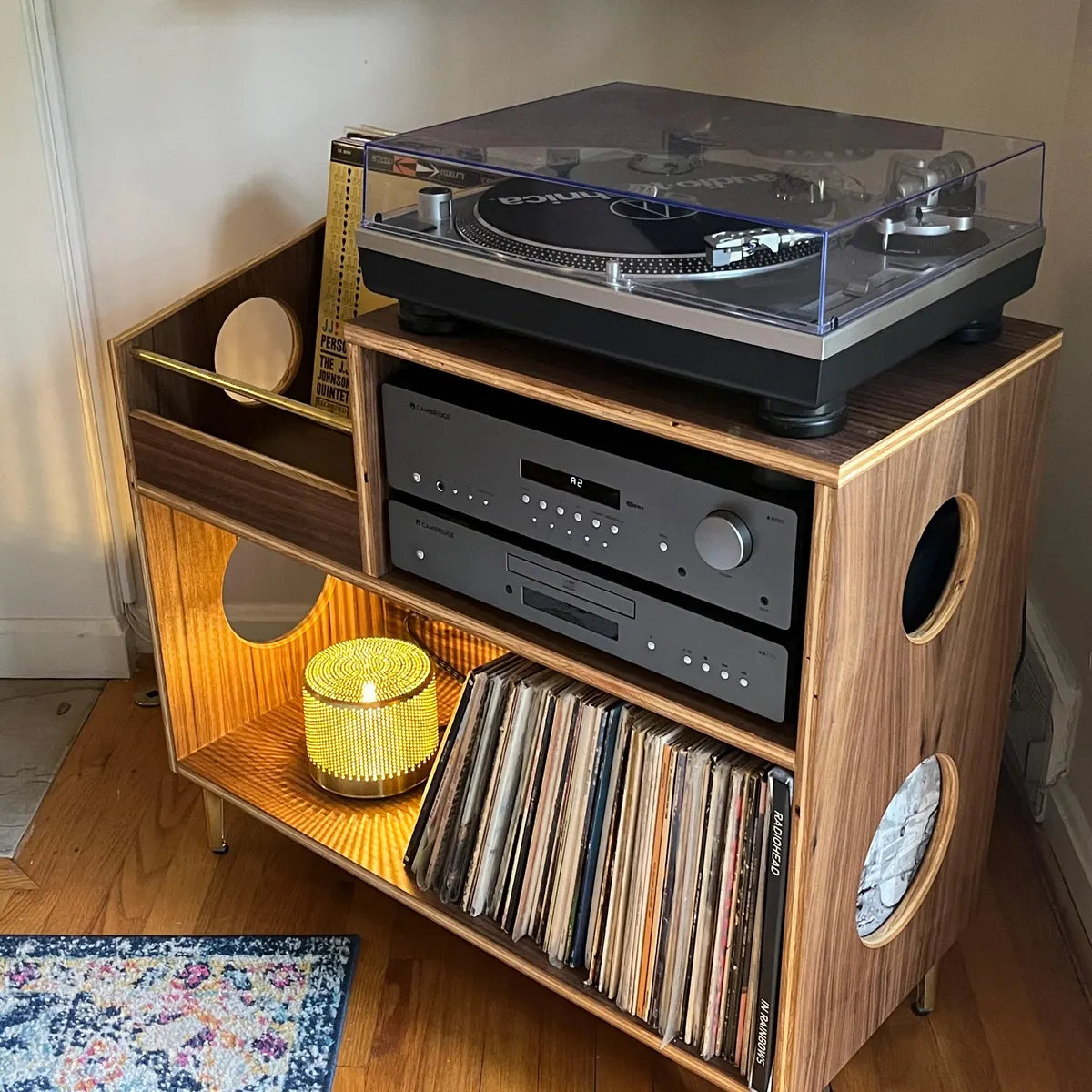 Wooden record player console with turntable, speakers, and vinyl records on a wooden floor.